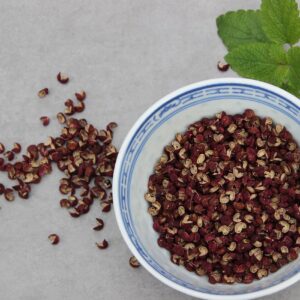 A decorative bowl containing the seed husks of Zanthoxylum simulans, complemented by two small sprigs of something in the mint family.