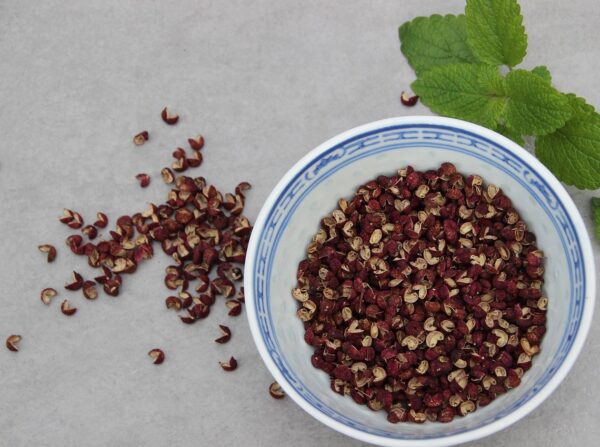 A decorative bowl containing the seed husks of Zanthoxylum simulans, complemented by two small sprigs of something in the mint family.